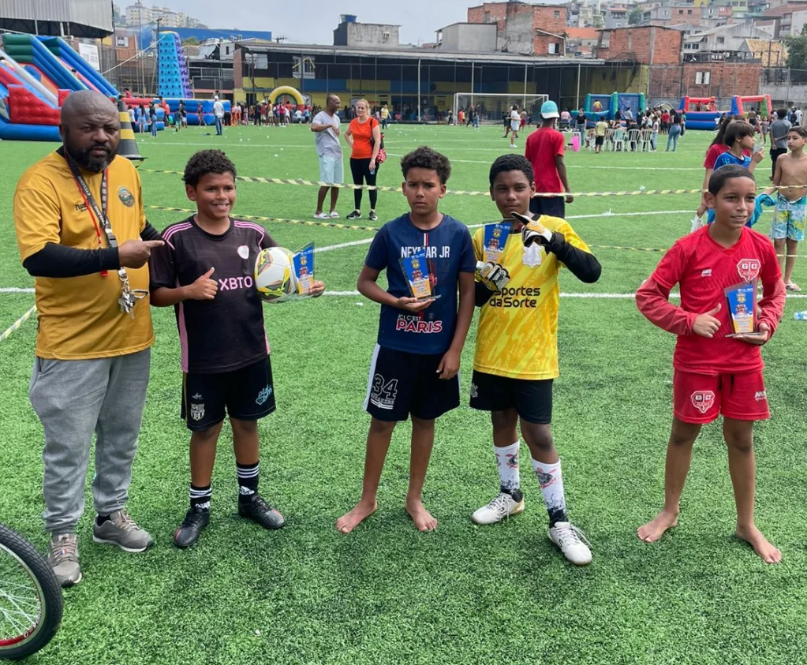 Um adulto e quatro jovens posam com lembranças em um campo durante um evento esportivo.