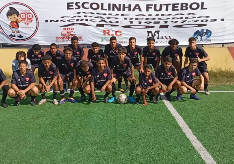 Grupo de jovens reunido para uma foto em um campo de futebol, com uma faixa ao fundo.